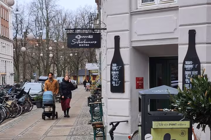 Couple strolling past Silberbauers Bistro on a picturesque Copenhagen street, perfect for exploring Danish culture.
