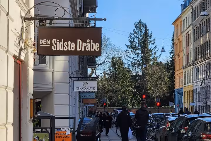 Charming Copenhagen street with pedestrians and signs of local shops on a sunny day, ideal for a walking tour.
