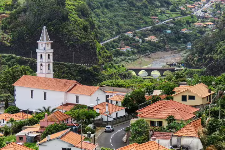 Scenic view of a charming village in Northeast Madeira with lush greenery, traditional architecture, and a picturesque bridge.