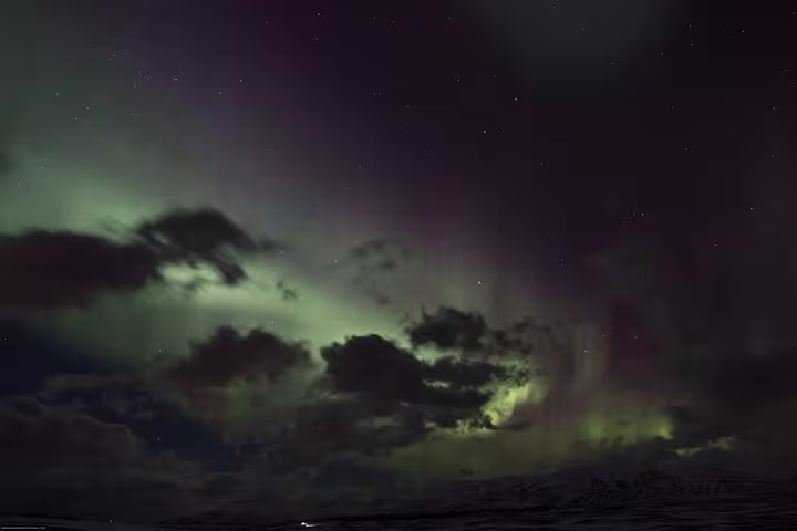 Majestic auroras illuminate the night clouds above Akureyri on a thrilling 4x4 Northern Lights tour.