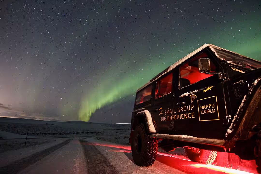 Small-group 4x4 aurora tour vehicle on snowy road under Northern Lights and starry sky, prime stargazing adventure