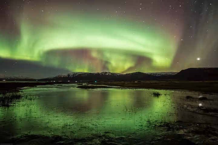 Vibrant aurora borealis reflecting in a serene lake near Akureyri, ideal for Northern Lights 4x4 tour exploration.