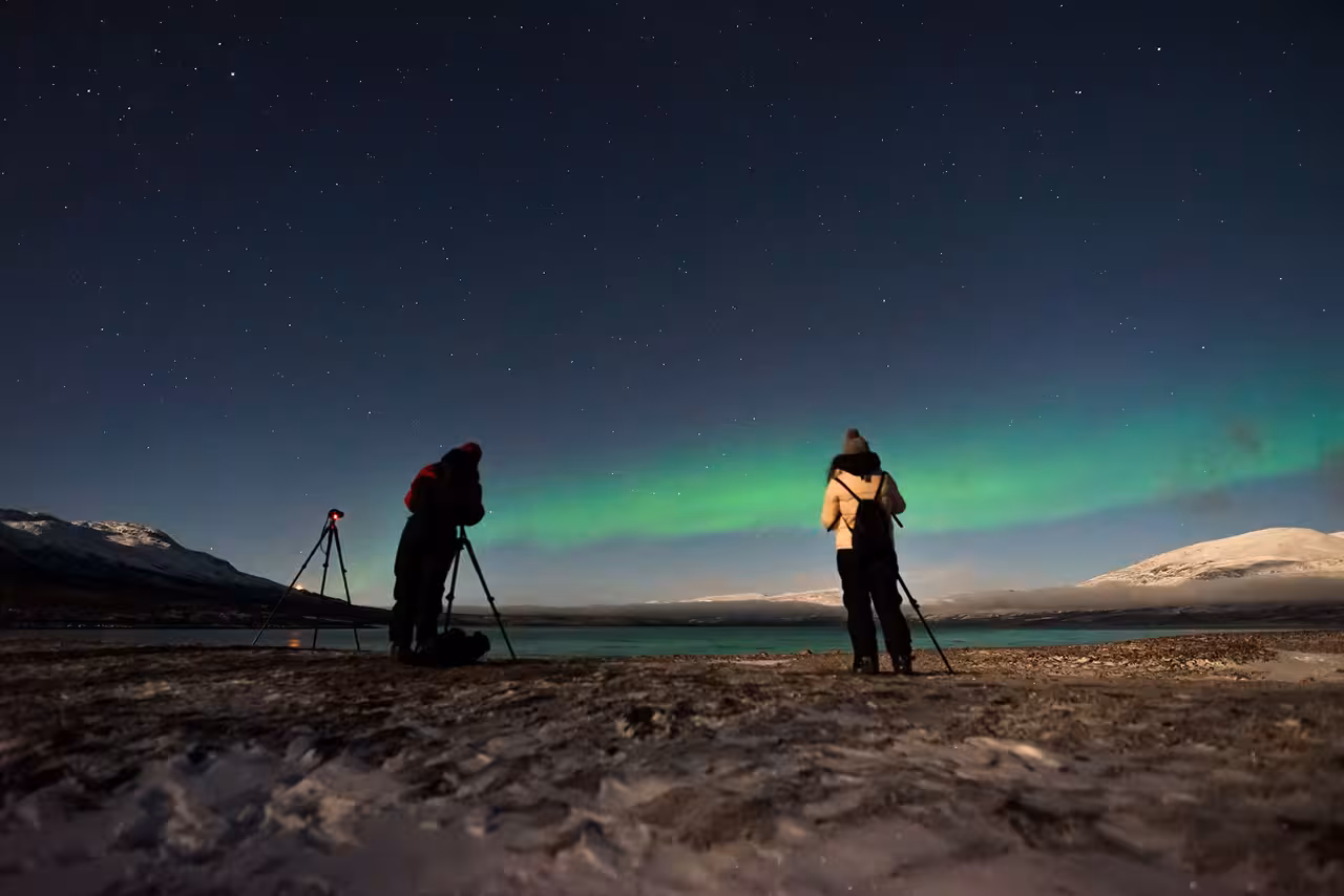 Photographers capture the Northern Lights on a snowy private tour, with vibrant auroras lighting up the night sky.