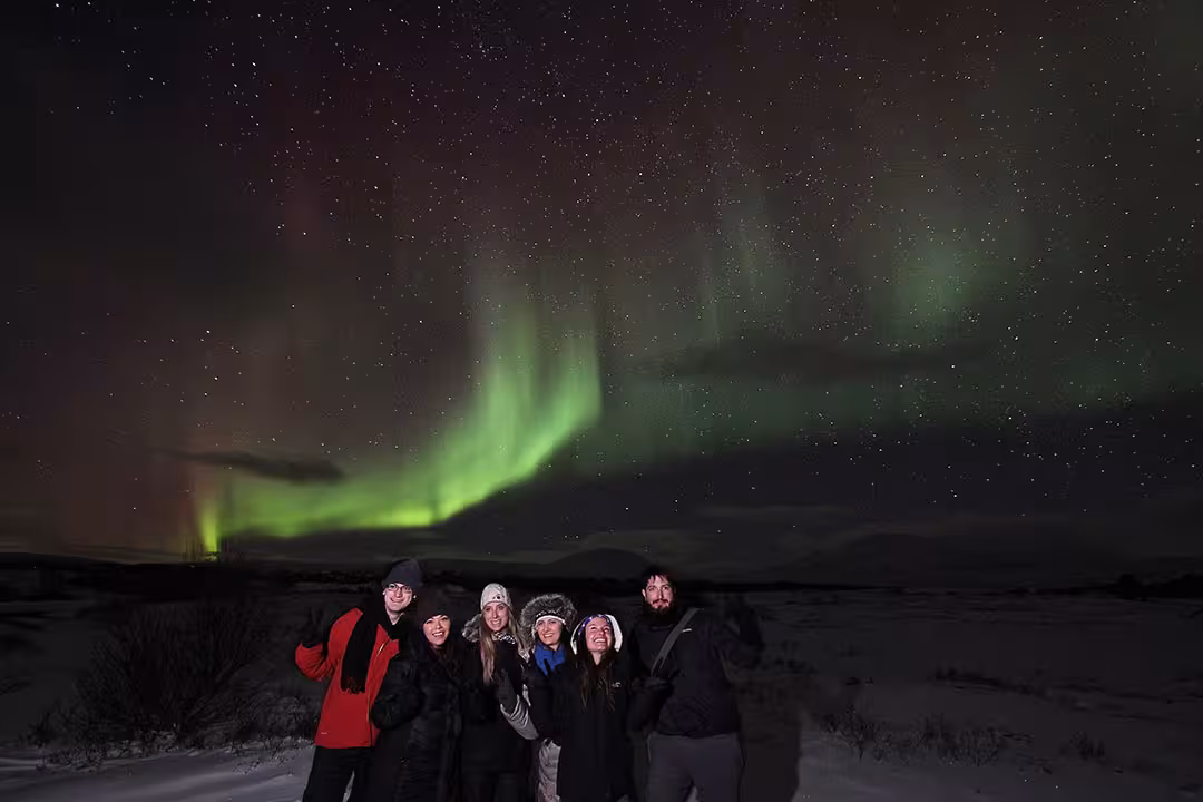 Group posing beneath vivid green aurora and stars on a winter night, Northern Lights and stargazing tour