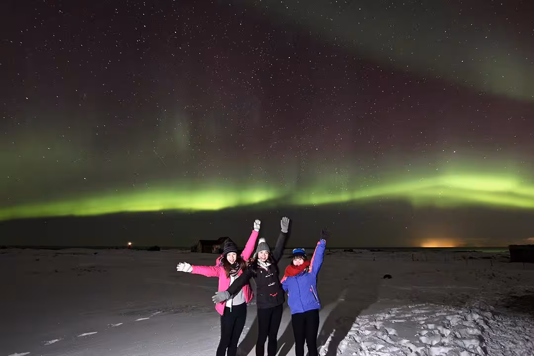 Travelers celebrate under green Northern Lights on a snowy night, perfect aurora and stargazing tour photo stop