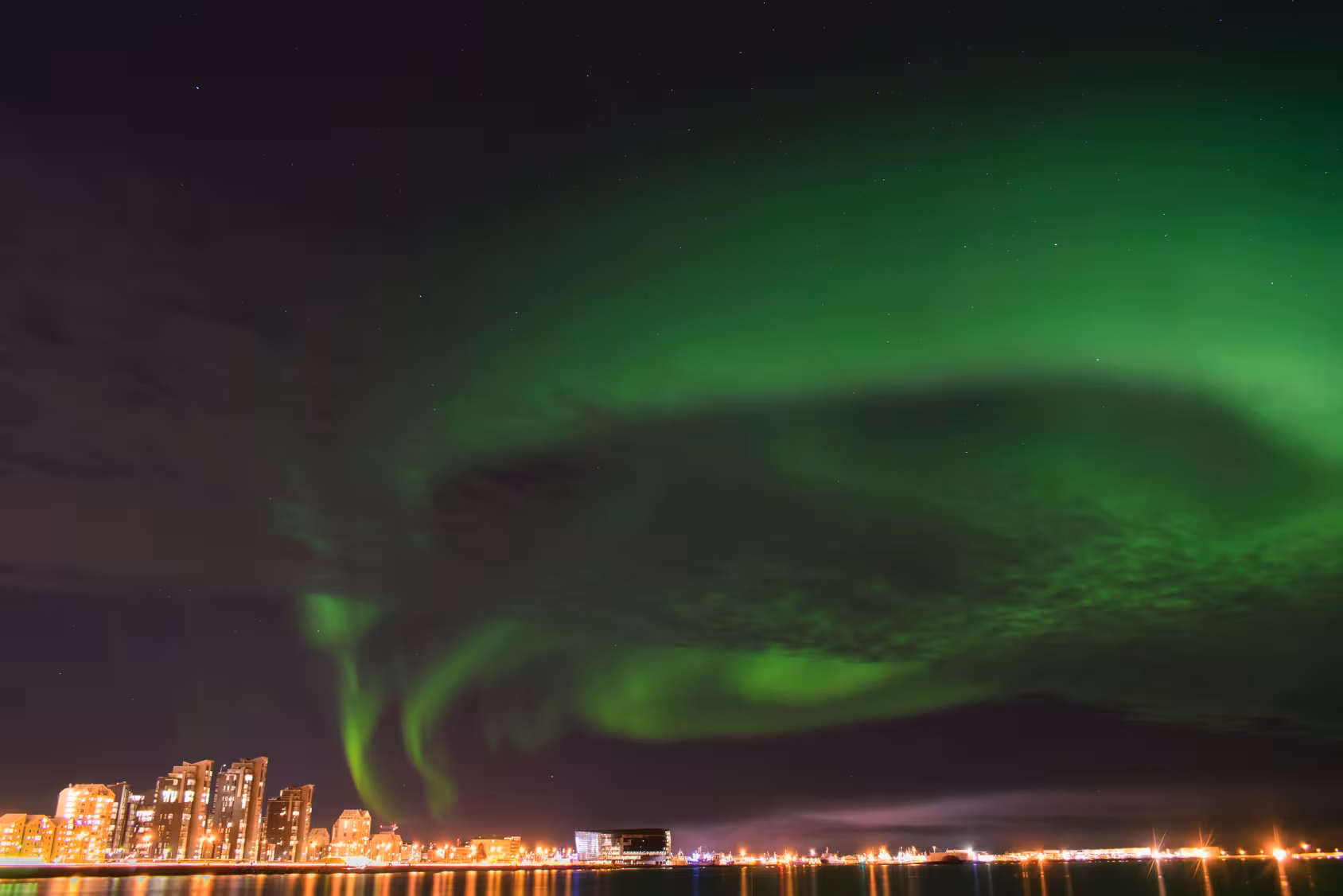 Stunning view of Northern Lights over Reykjavík cityscape, perfect for a 3-night Icelandic adventure.