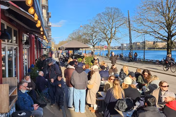 People enjoying outdoor cafes by Copenhagen lakeside under clear blue skies on a walking tour.