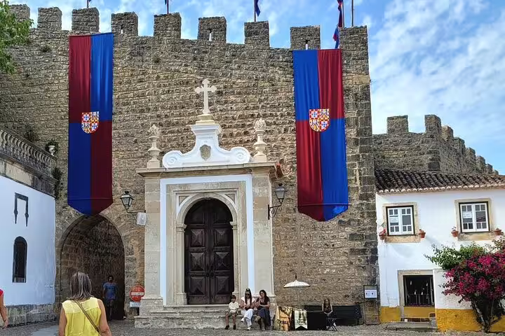 Historic castle entrance in Óbidos adorned with Portuguese flags, a highlight of the Fatima-Nazare-Obidos tour.