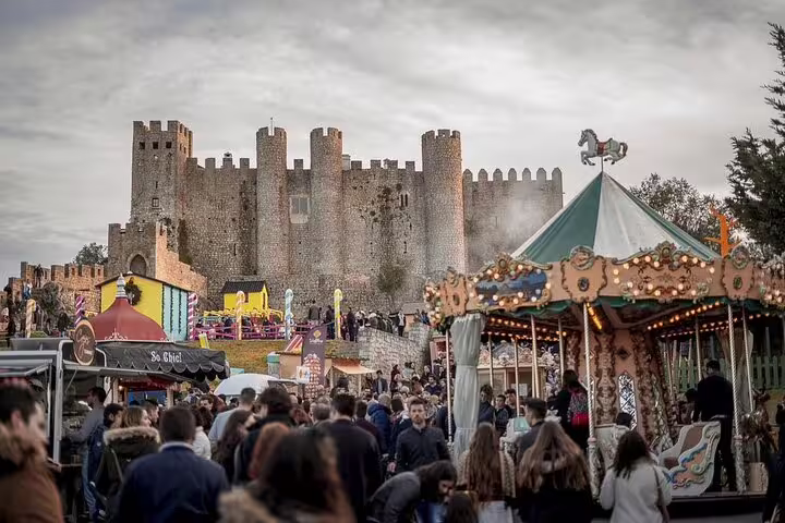 Vibrant festival scene at Óbidos Castle with bustling crowds and a colorful carousel, showcasing Portugal's lively culture.