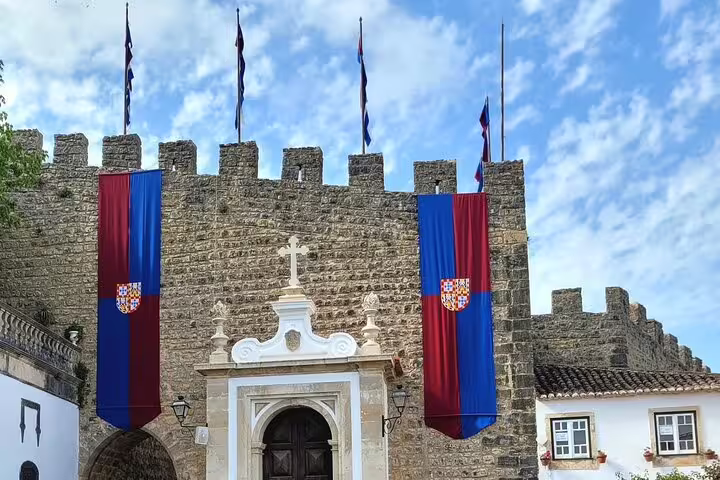 Historic castle adorned with vibrant flags in Óbidos, featured in Tomar-Coimbra and Fatima-Nazare-Obidos tour.