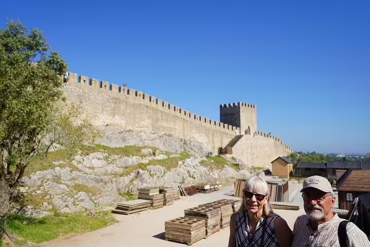 Tourists explore the historic Óbidos Castle under a clear blue sky on a full-day private tour from Lisbon.