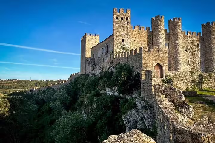 Majestic medieval Óbidos Castle under a clear blue sky, featured on the Fátima, Nazaré, and Óbidos full-day tour.