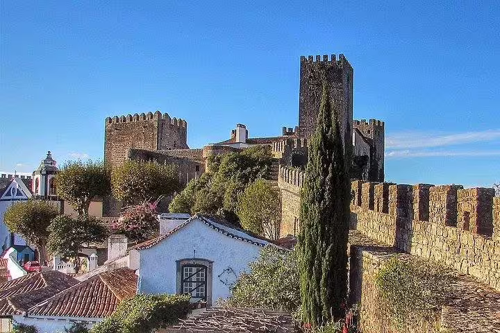 Scenic view of Óbidos Castle with its fortified walls and lush greenery on a sunny day.