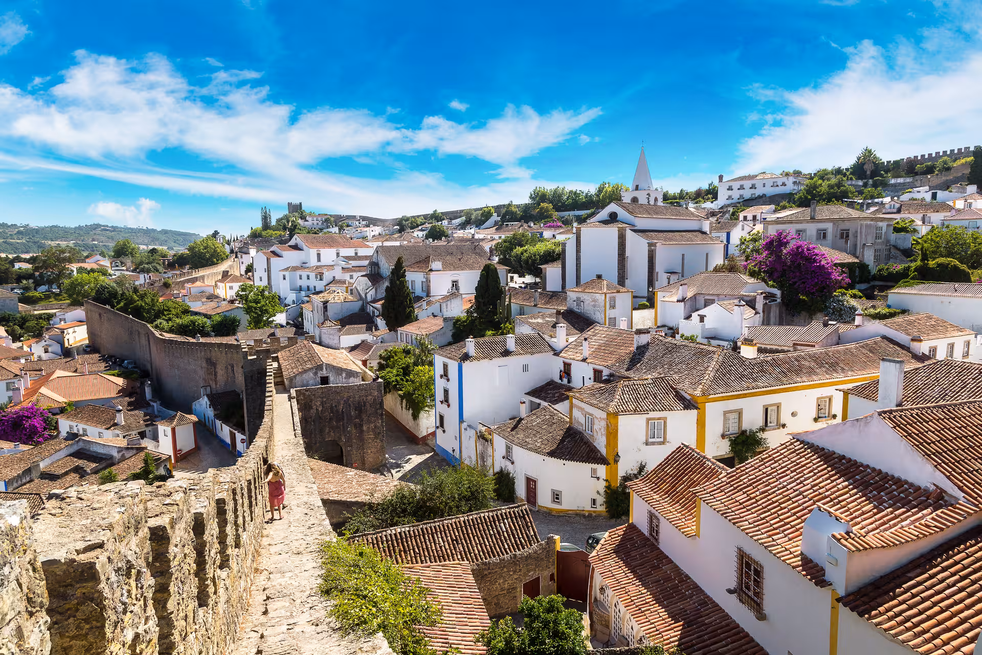 Scenic view of Óbidos from castle walls, showcasing historic rooftops, whitewashed houses, and vibrant bougainvillea.