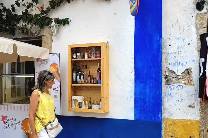 Charming street scene in Obidos with a woman admiring a vibrant wall and local products on a Fatima-Nazare-Obidos tour.