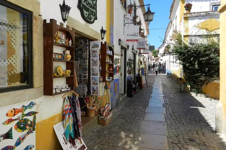 Charming cobblestone street in Óbidos, Portugal, showcasing vibrant local shops and colorful ceramics on a small group day tour.