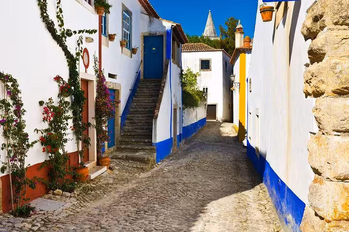 Charming cobblestone street in Óbidos with colorful houses adorned with flowering vines.