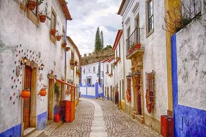 Charming cobblestone street in Óbidos lined with colorful traditional houses adorned with potted plants.