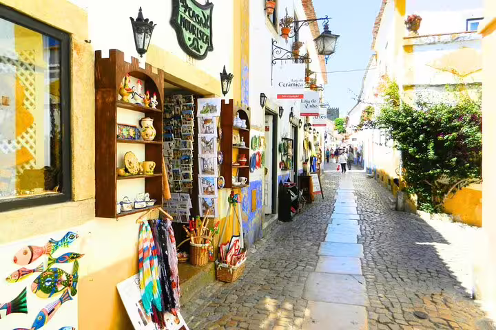 Charming cobblestone street in Óbidos lined with colorful shops and traditional crafts, part of a small group tour from Lisbon.