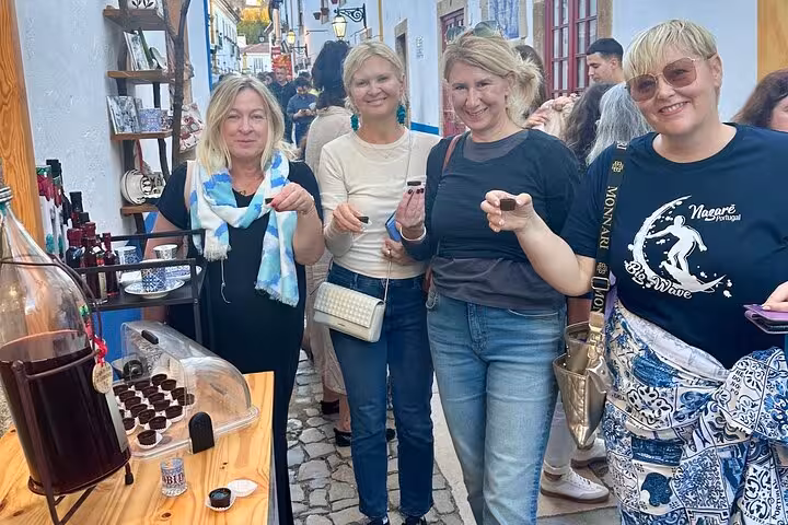 Tourists savoring local beverages in the charming streets of Obidos on a private car tour.