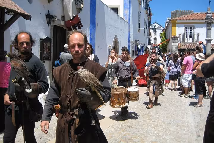 Medieval festival in Óbidos featuring performers with birds and musicians in a cobblestone street setting.