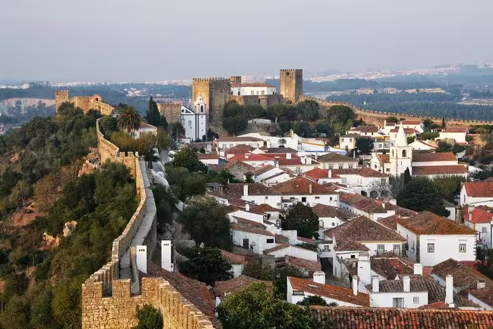 Scenic view of Óbidos village with medieval walls and castle, featuring charming white houses and lush greenery, perfect for a private tour from Lisboa.