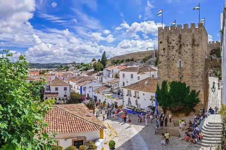 Charming medieval village of Óbidos with cobblestone streets and a historic castle under a vibrant blue sky.