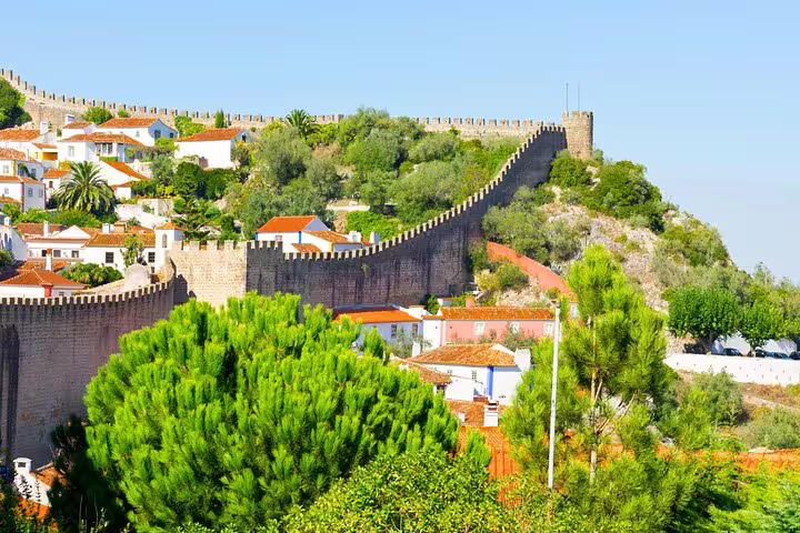 Scenic view of Óbidos with medieval walls and lush greenery, featured in Lisbon's small group day tour to Fátima, Nazaré.