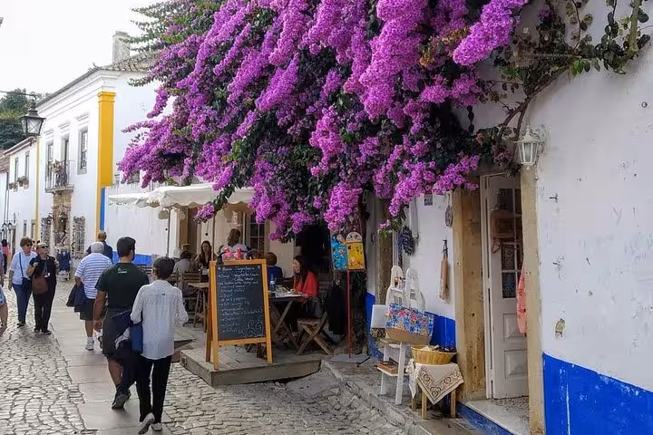 Charming Óbidos street with vibrant purple bougainvillea and quaint café, perfect for a private Portugal tour.