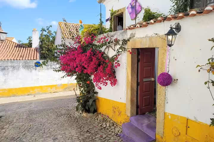 Charming Óbidos street with vibrant bougainvillea and colorful house, perfect for a Fátima, Batalha, Nazaré, Óbidos tour.