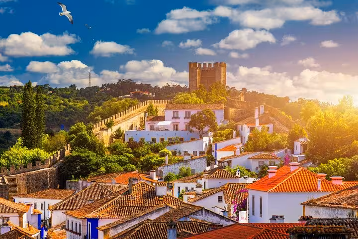 Scenic view of Óbidos village with medieval castle walls and lush greenery under a vibrant sky.