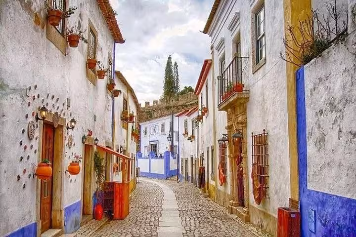 Picturesque street in Óbidos lined with whitewashed houses, vibrant accents, and cobblestone path leading to a castle.