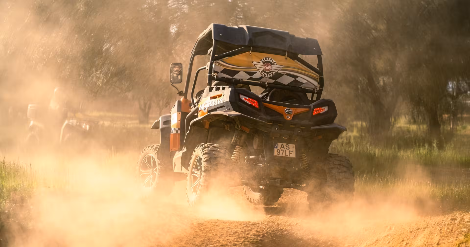 Rear view of off-road buggy kicking up dust on a guided half-day tour, exploring rugged Algarve countryside tracks at sunset