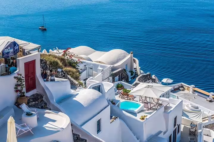 Oia cave houses and infinity pool above the blue caldera, featured on a private 2-hour Santorini sightseeing tour