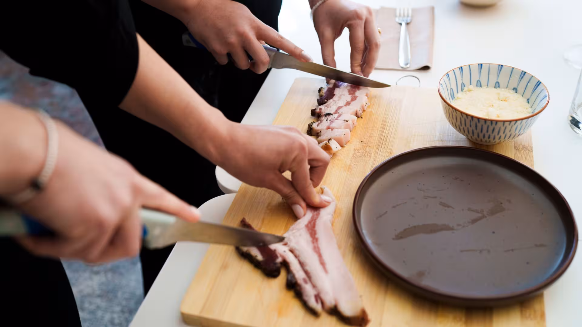Participants slicing pancetta for authentic pasta carbonara during Olbia's interactive cooking class experience.