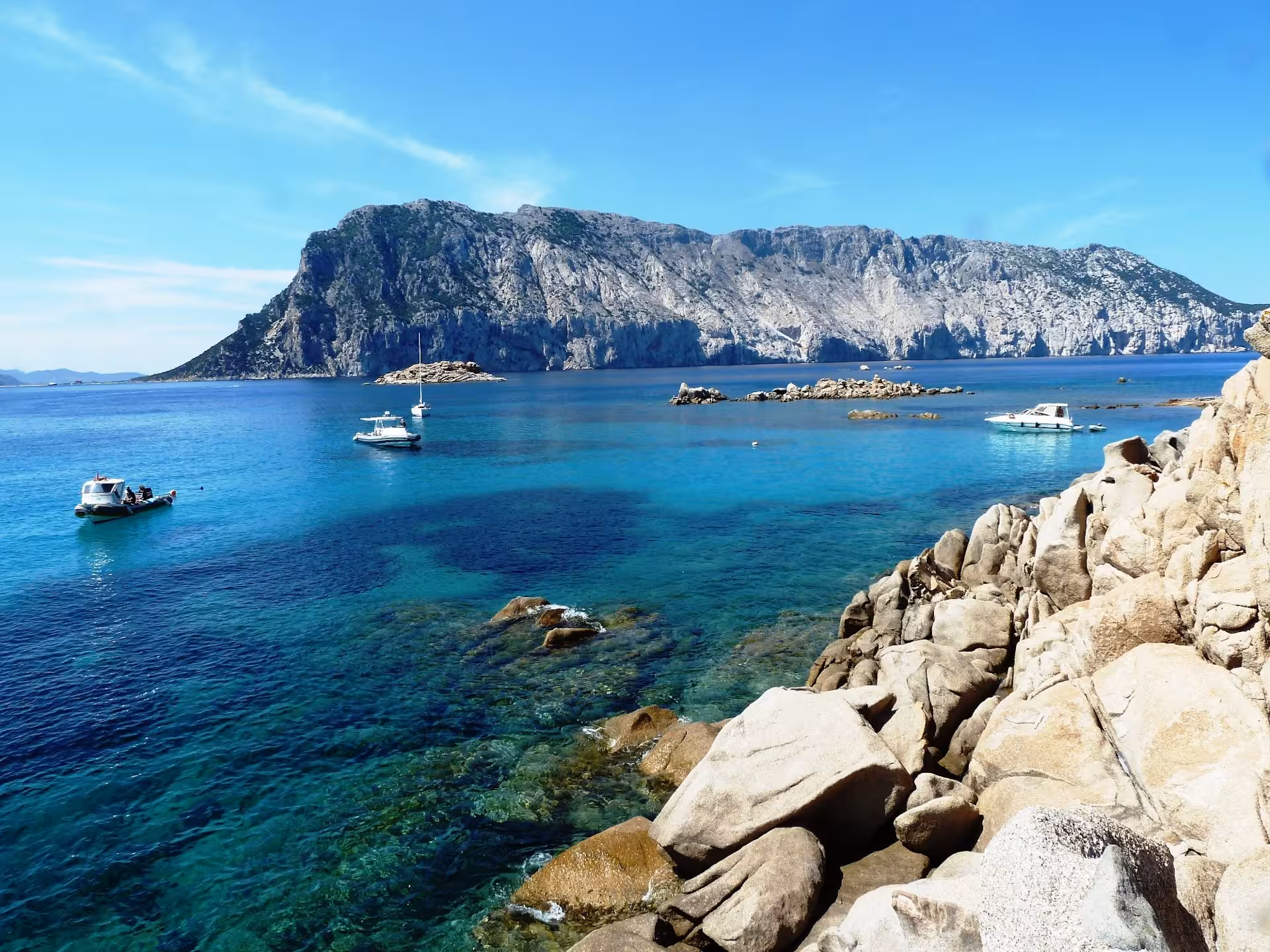 Dinghies and boats anchored near Tavolara Island's rocky coastline, showcasing Sardinia's stunning seascape.