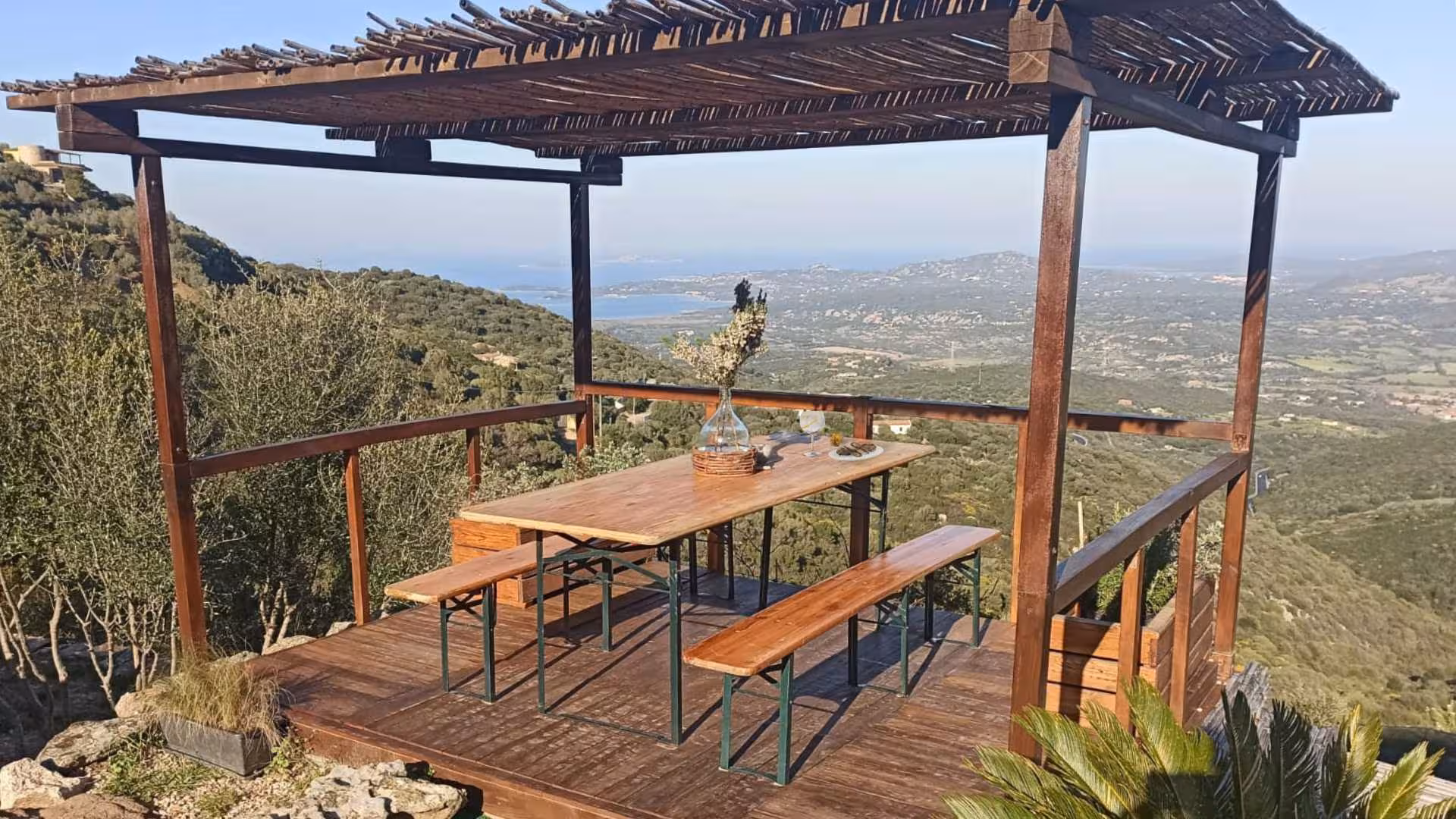 Scenic view from a rustic wooden terrace overlooking Olbia's lush landscape, ideal for gin tasting experiences.