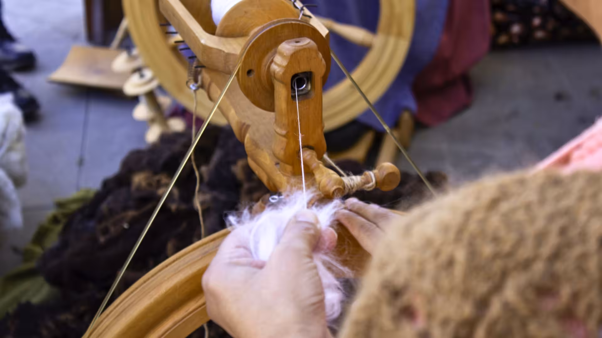 Close-up of hands spinning wool on a wooden wheel, highlighting Olbia's traditional wool crafting techniques.