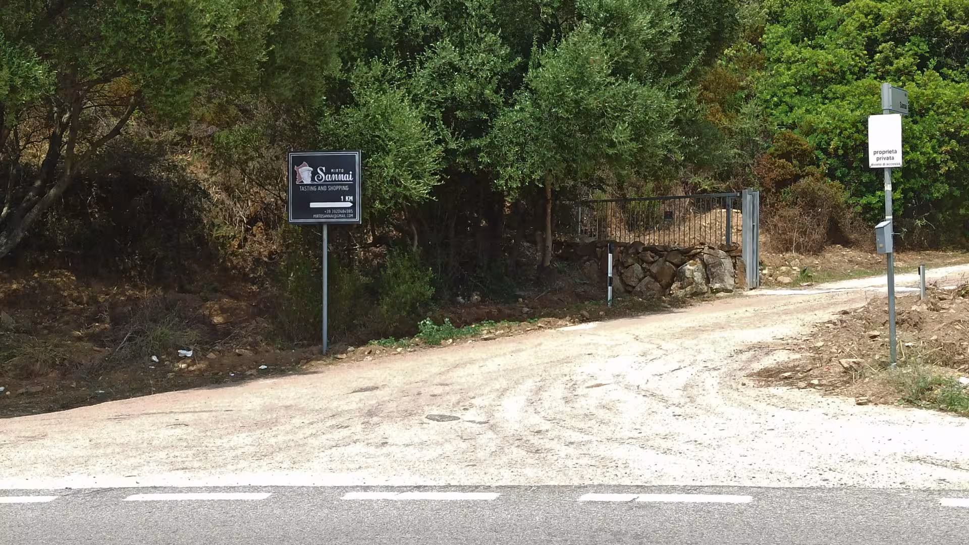 Entrance to myrtle-making factory in Olbia with sign for tasting and shopping, surrounded by lush greenery.