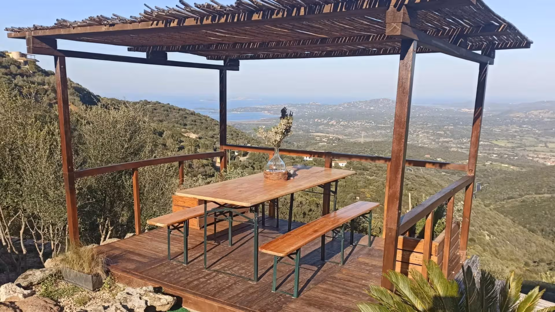 Scenic wooden terrace overlooking Olbia's lush hills, perfect for a myrtle tasting experience.
