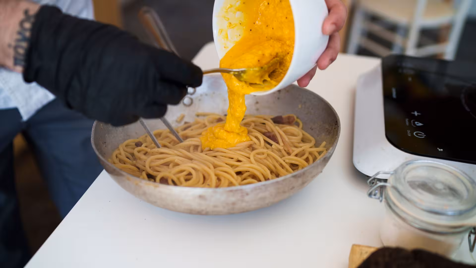 Rich egg yolk sauce being poured over spaghetti in Olbia's traditional pasta carbonara cooking class.