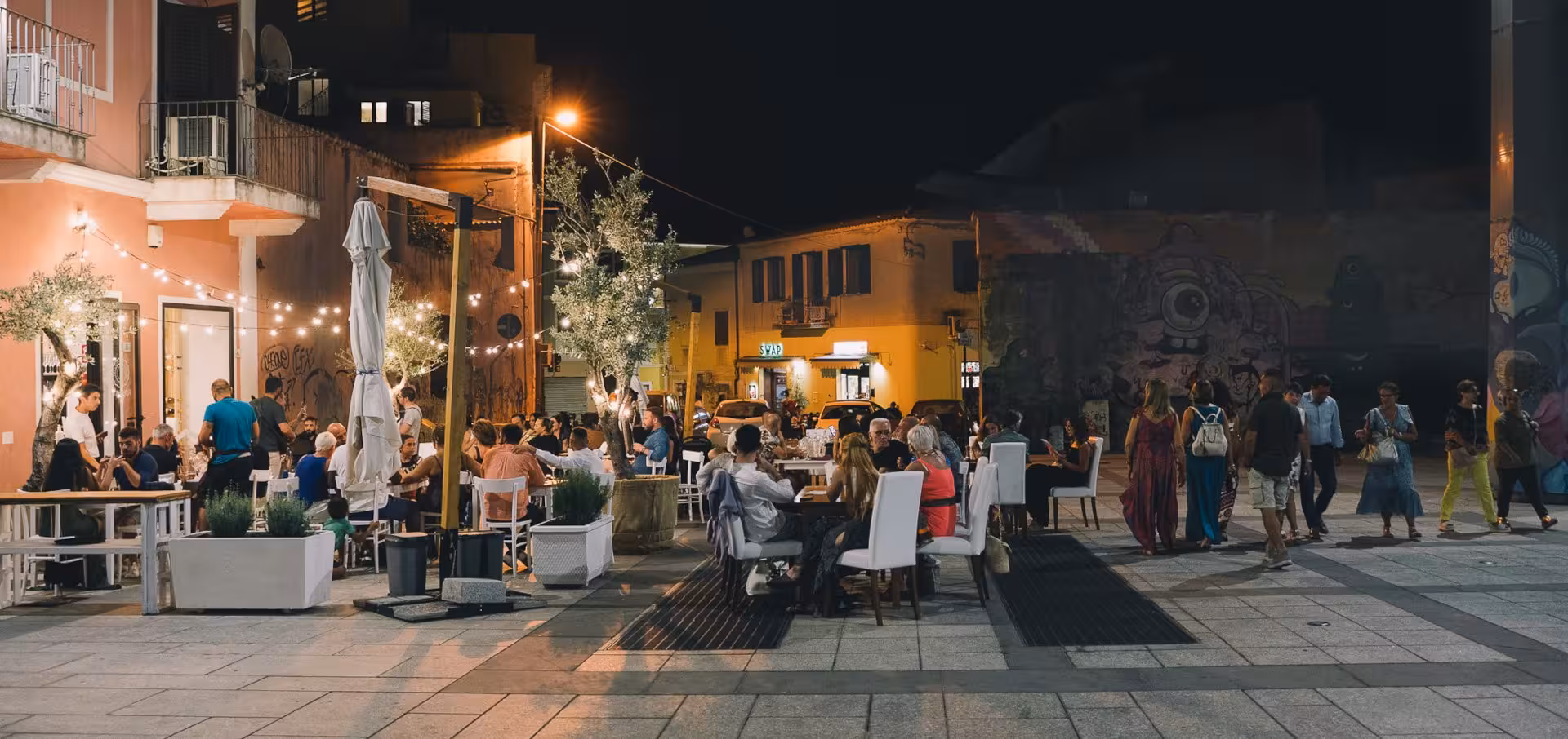 Vibrant Olbia evening with diners enjoying local cuisine under twinkling lights in a charming outdoor setting.