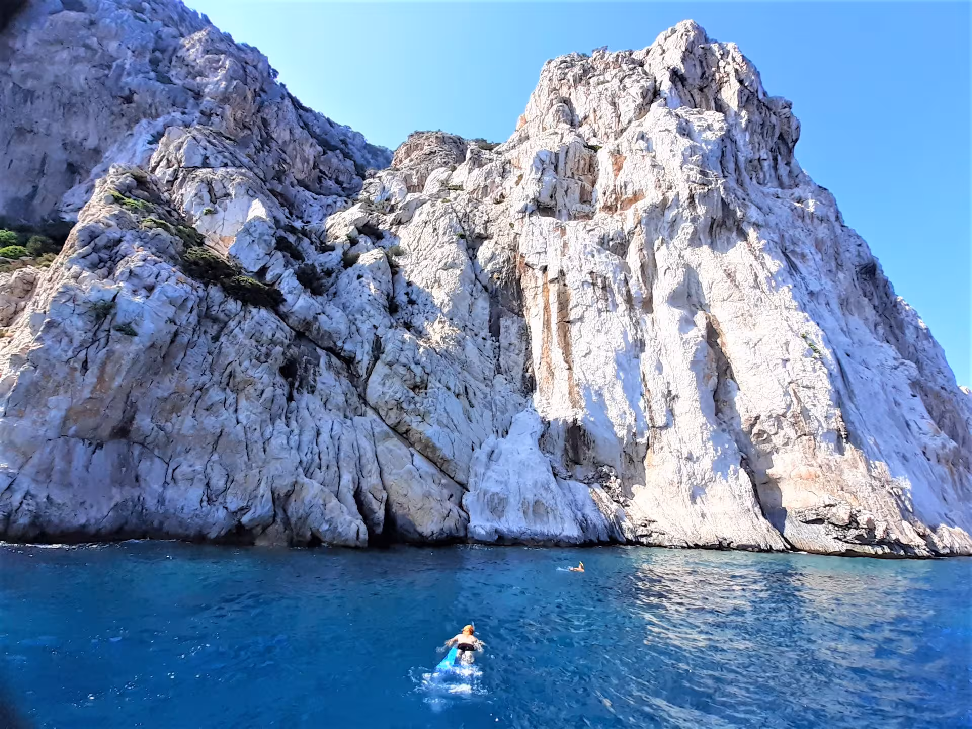 Swimmer exploring the crystal-clear waters near the towering cliffs of Capo Figari on a RIB tour from Olbia.