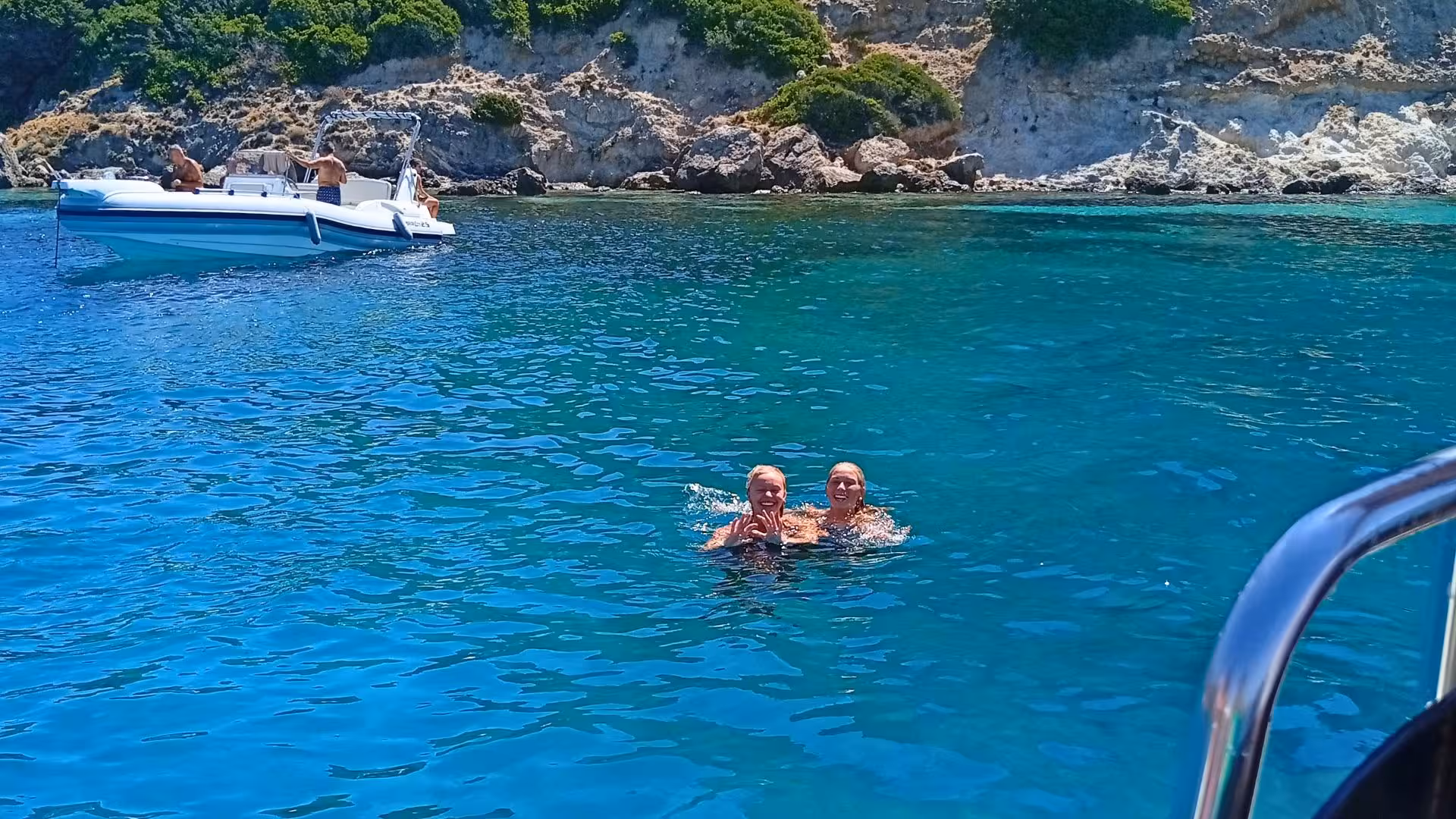 Two people swimming in turquoise waters near a RIB boat at Capriccioli, highlighting Olbia's coastal tour attractions.