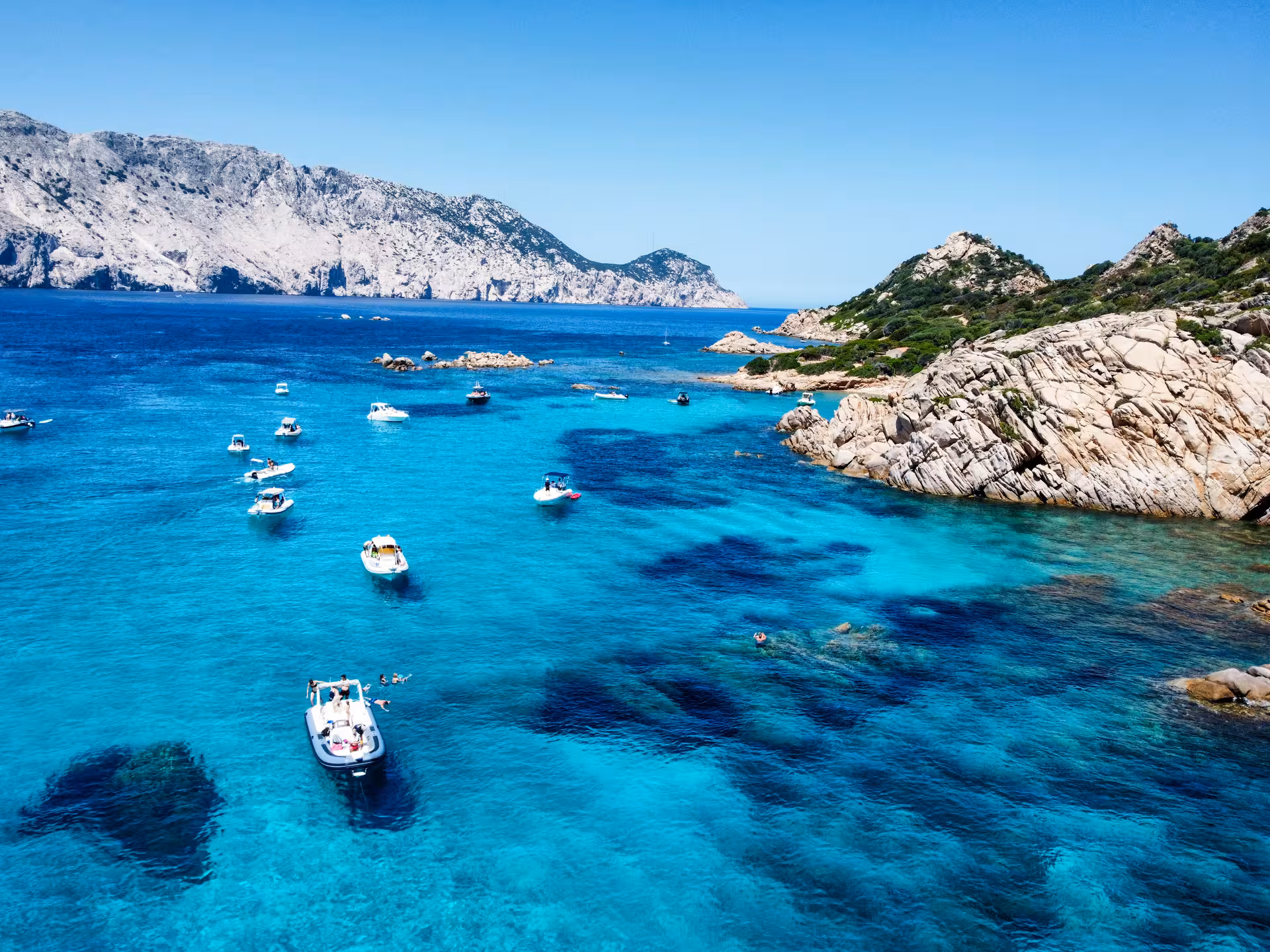 Aerial view of boats anchored in the turquoise waters near the rocky shores of Tavolara and Cala Moresca.