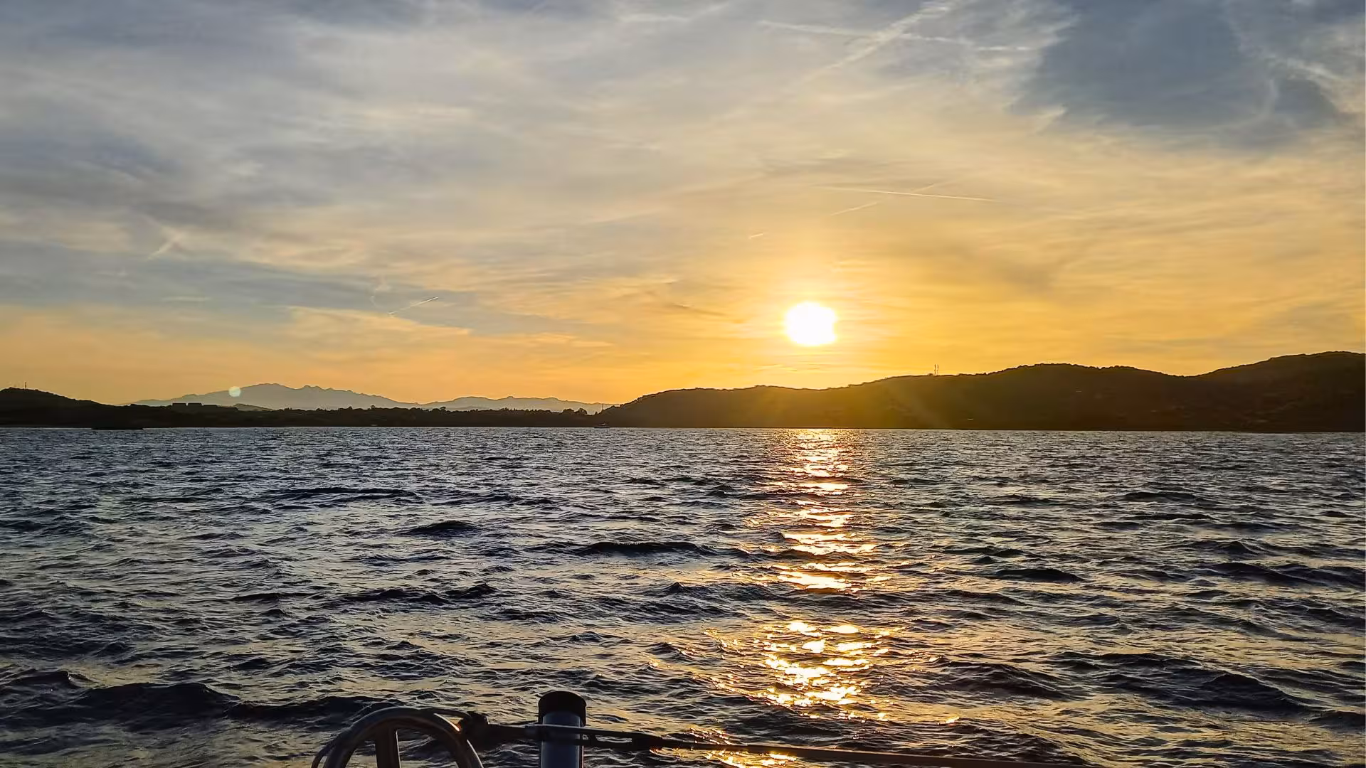 Golden sunset over the sea with gentle waves near Olbia, viewed from a catamaran.