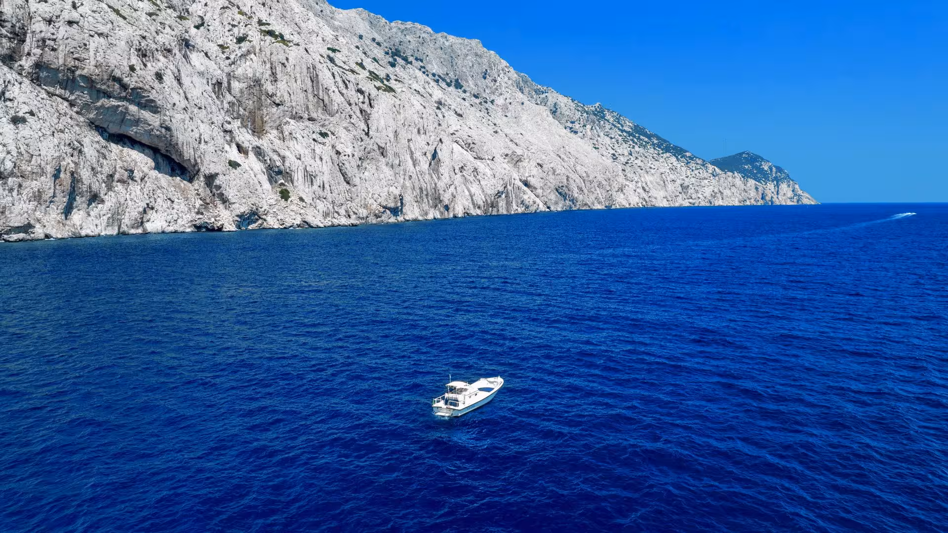 Small boat on deep blue sea with rugged cliffs of Tavolara Island, Porto San Paolo tour.
