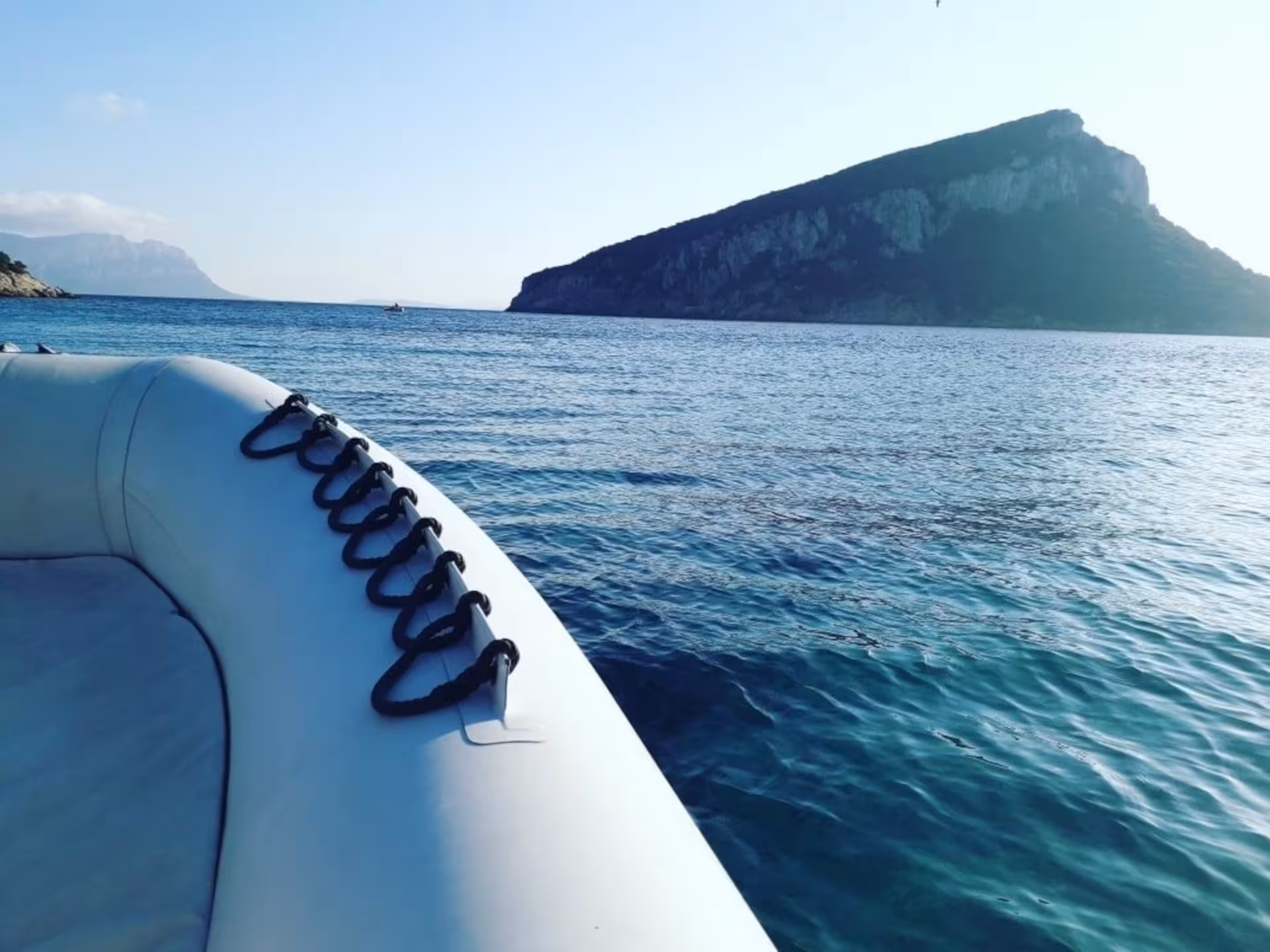 Scenic view from a boat approaching Tavolara Island, showcasing clear blue waters and rugged coastline.