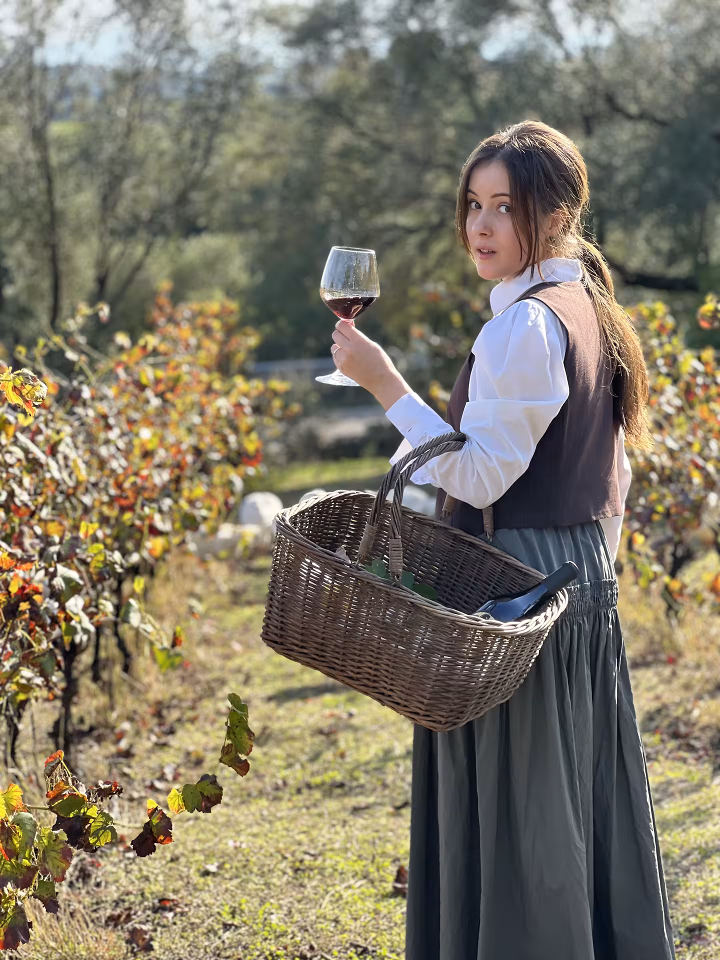 Woman enjoying wine with a basket in a picturesque Olbia vineyard under a clear sky.
