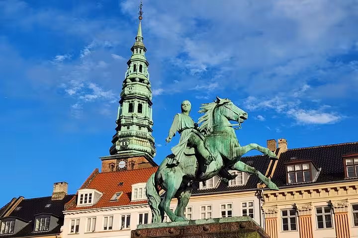 Historic equestrian statue and iconic spire against a clear blue sky in Old Copenhagen.